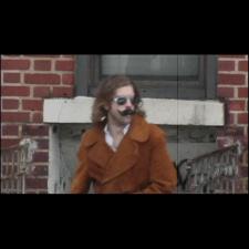 A man with a moustache and glasses standing in front of a building